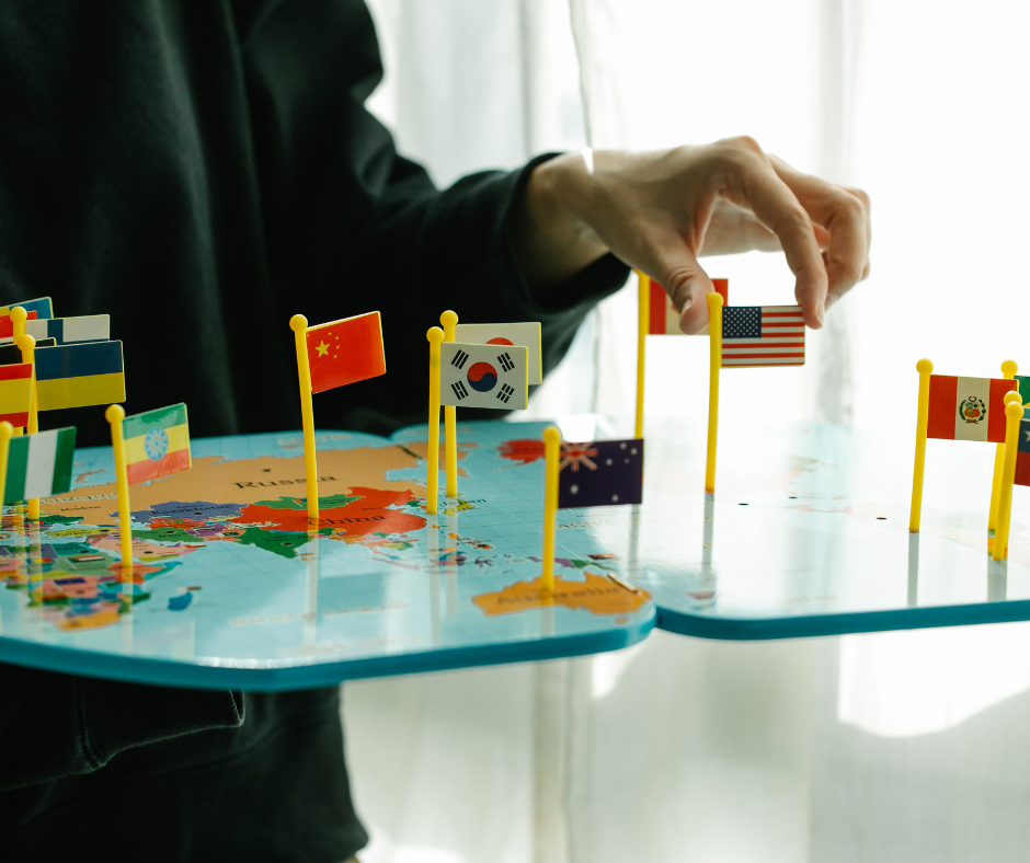 A person placing small national flags, including the U.S., China, and South Korea, on a colorful world map, symbolizing global communication and international connections.