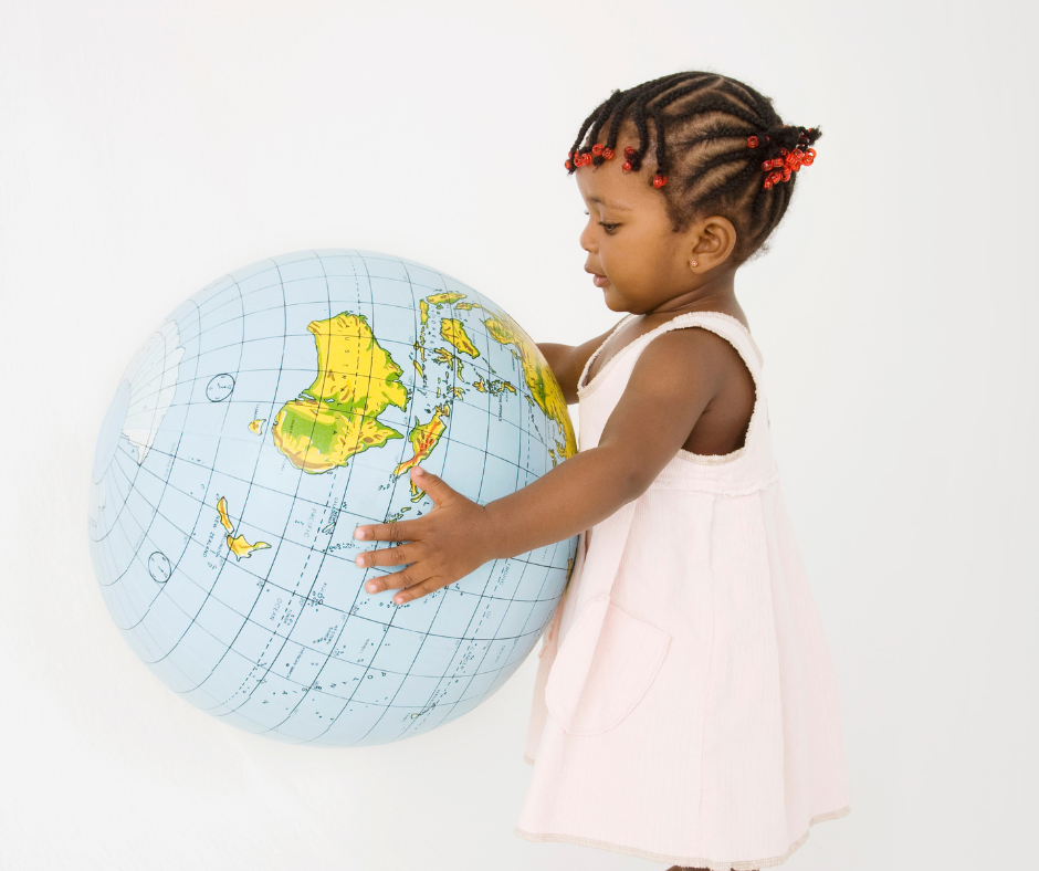 Toddler in a pink dress holding a large inflatable globe against a white background.